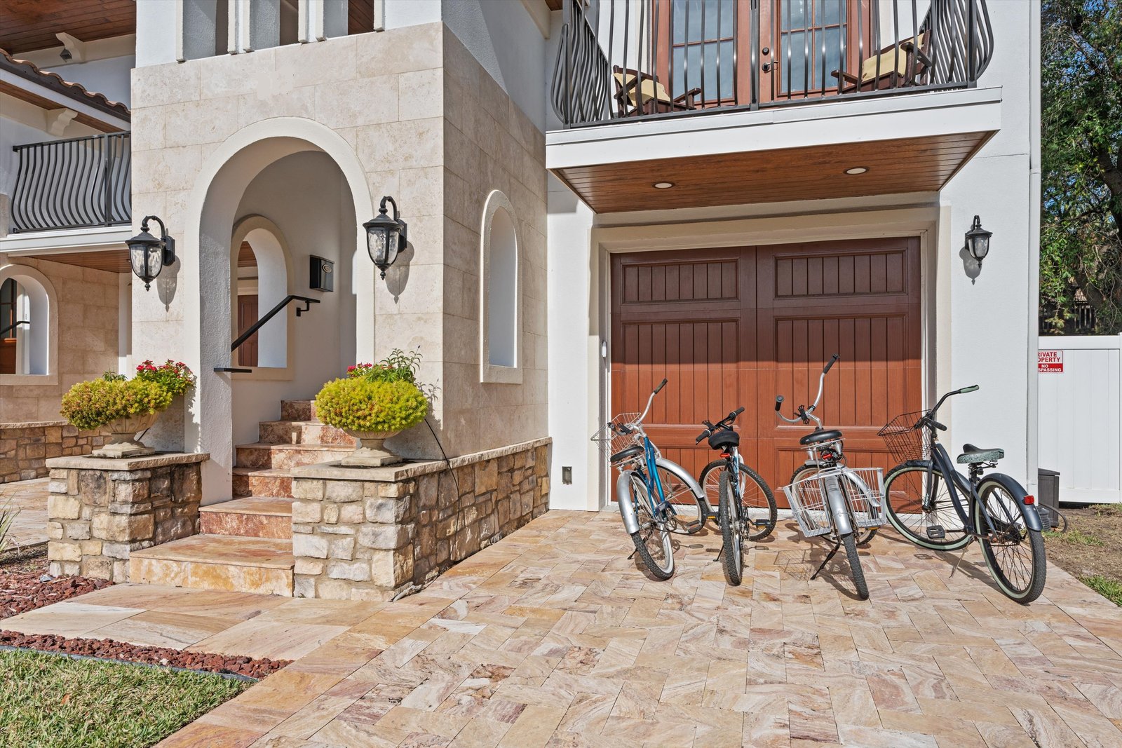 Stone-and-stucco beach house entry with arched stairway and four beach cruisers parked by the garage